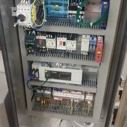 Eco Volt Energy Marek Pietraszkiewicz - Rozdzielnica elektryczna w metalowej obudowie z widocznymi elementami sterującymi, przewodami i zabezpieczeniami. Widoczne komponenty Mitsubishi.