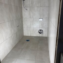 Marcin - Wykończona kabina prysznicowa z beżowymi płytkami, widoczny odpływ liniowy, instalacja prysznicowa i elektryczna. Minimalistyczny design, jasne wnętrze.