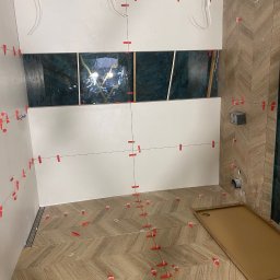 Marcin - Łazienka w trakcie prac: ułożona podłoga w jodełkę, białe ściany z poziomymi liniami i czerwonymi klipsami, fragment zielonej ściany. Widoczne kable i otwory.