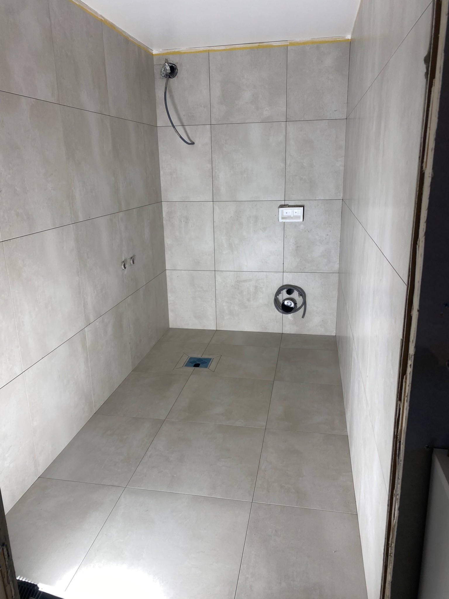 Wykończona kabina prysznicowa z beżowymi płytkami, widoczny odpływ liniowy, instalacja prysznicowa i elektryczna. Minimalistyczny design, jasne wnętrze.