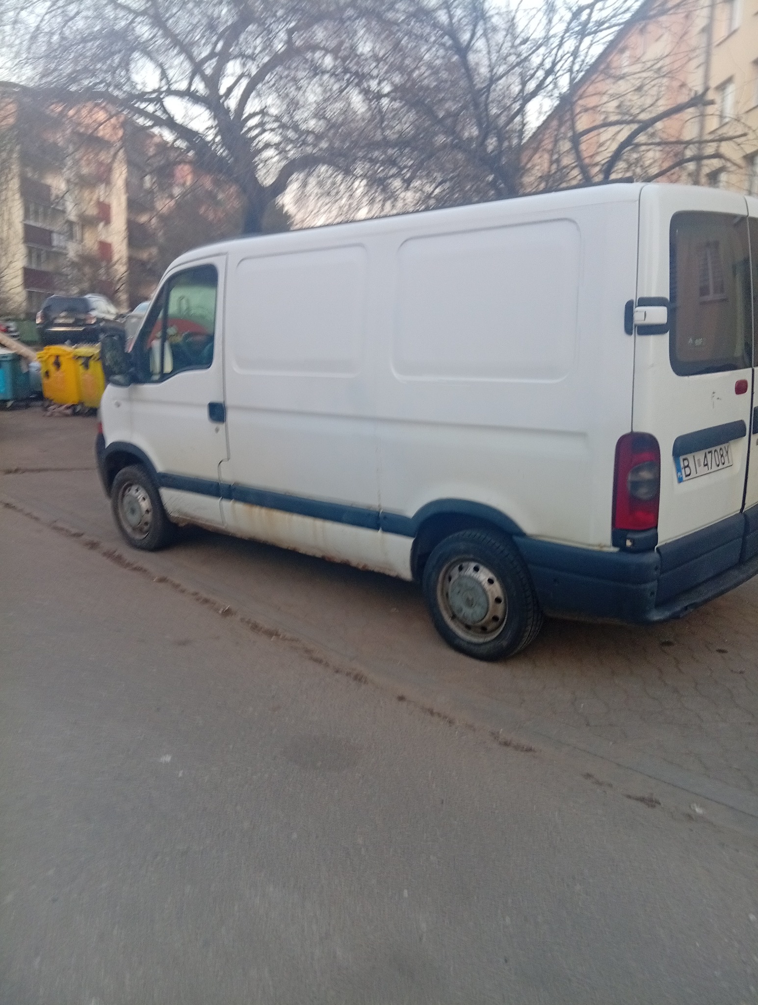 Biały, lekko zabrudzony bus dostawczy Renault Master zaparkowany na ulicy w mieście, widok z boku, z widoczną tablicą rejestracyjną.