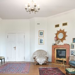 Adam Neubauer FOTOGRAFIA - Salon w stylu retro z kominkiem, turkusową sofą i lustrami w złotych ramach. Na ścianach wiszą obrazy, a podłogę zdobią orientalne dywany. Centralnie umieszczony fotel z narzutą.