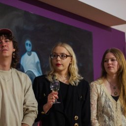 Danylo Vasiur - Grupa młodych osób pozuje na tle fioletowej ściany z obrazem. Kobieta w okularach trzyma kieliszek. Uwagę zwraca ekspresja i stylizacja.