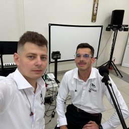 Łukasz Chełminiak Ratownictwo Medyczne i Usługi Pielęgniarskie - Dwóch muzyków zespołu Tonika Band w białych koszulach, z mikrofonami i sprzętem nagłośnieniowym w tle, gotowych do występu. Widoczny keyboard i oświetlenie.