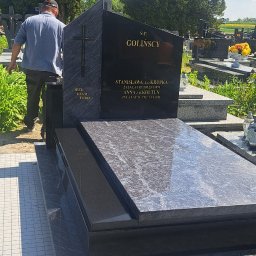 USŁUGI KAMIENIARSKIE I GRABARSKIE KORNEL DUDA - Czarny, polerowany nagrobek z szarego granitu na cmentarzu, z inskrypcjami i krzyżem. Mężczyzna w tle. Słoneczny dzień, widok na inne groby i zieleń.