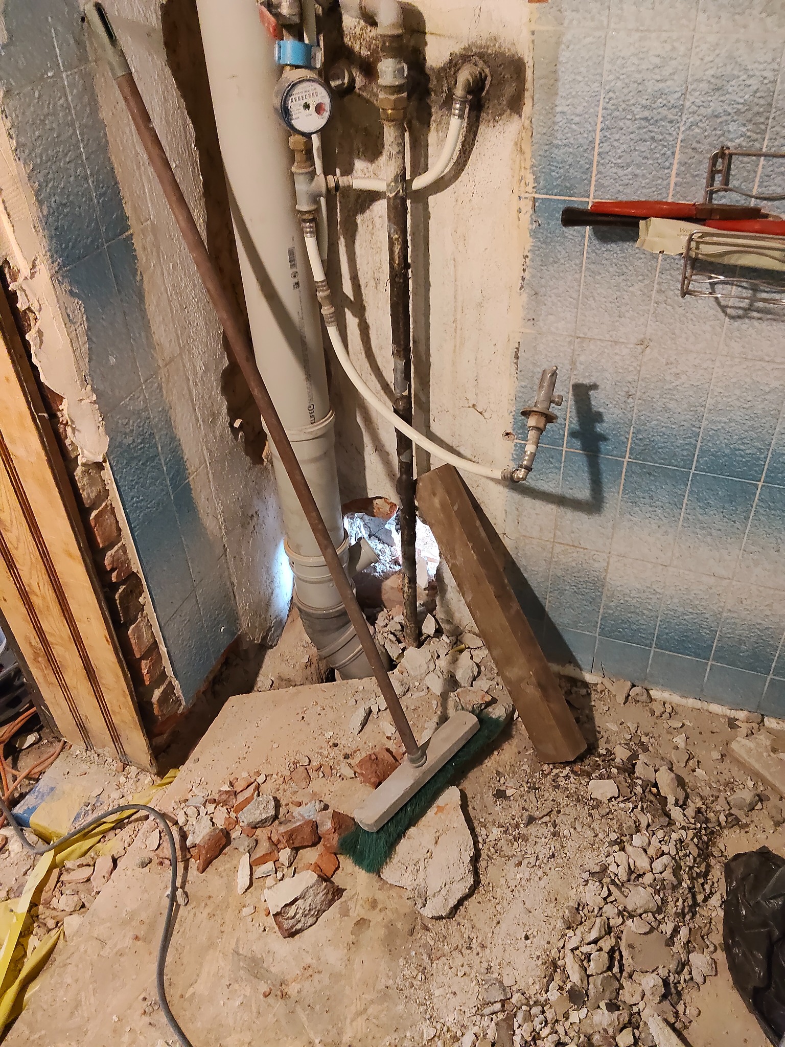 Demontaż starej instalacji wodnej w łazience z niebieskimi płytkami. Widoczne rury, gruz i narzędzia. Etap prac remontowych przed położeniem nowej instalacji.