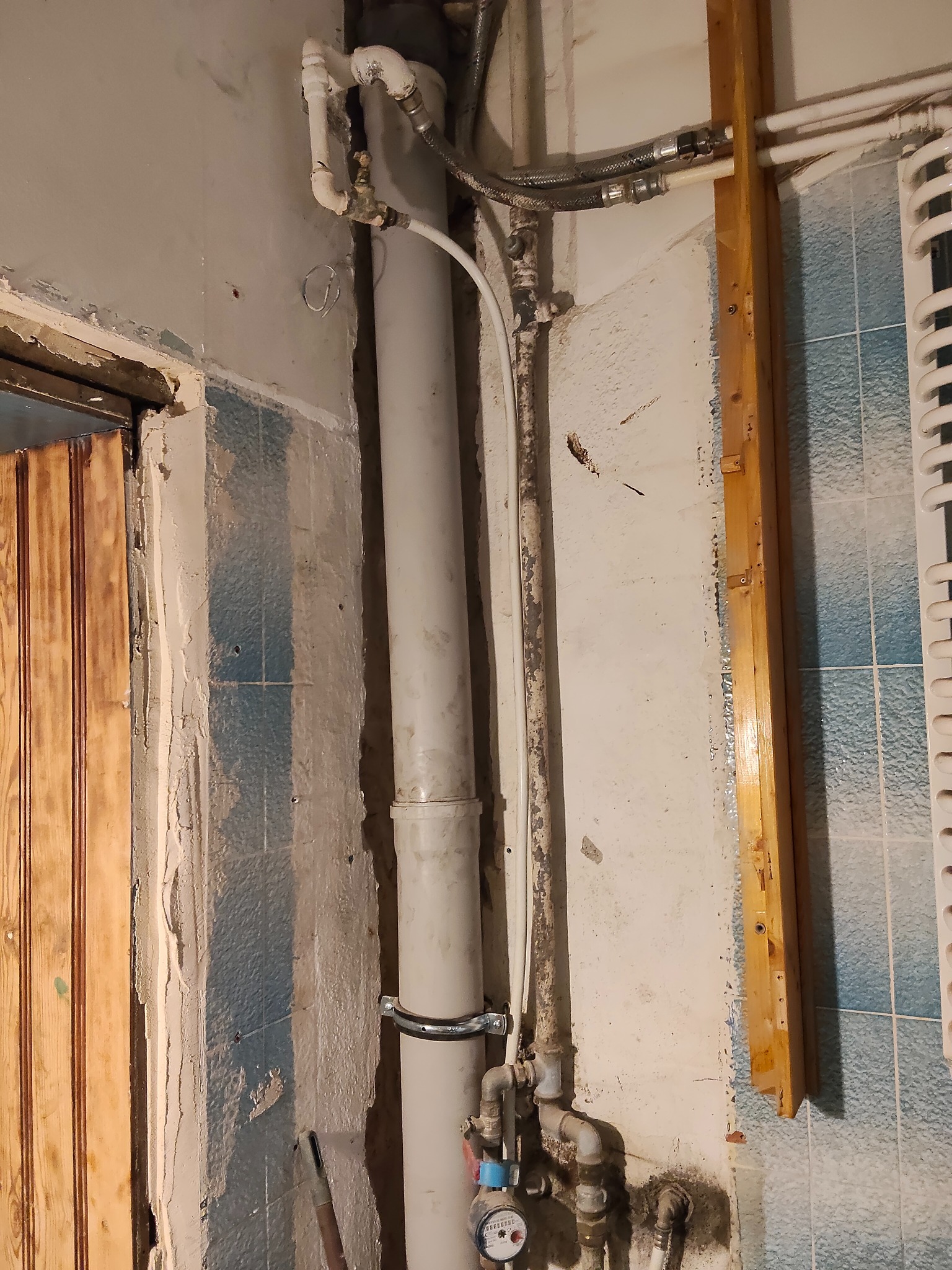 Rury wodne i kanalizacyjne w trakcie montażu w łazience z fragmentami starej glazury. Widoczne elementy instalacji i przygotowane ściany do dalszych prac wykończeniowych.