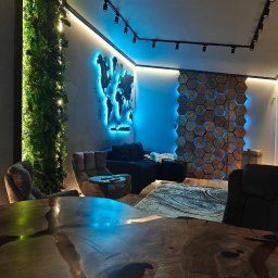 Roman Zhukov - Nowoczesne wnętrze z drewnianą ścianą w kształcie plastra miodu, podświetloną na niebiesko, oraz stołem z litego drewna z żywicą. W tle zielona ściana z mchu.