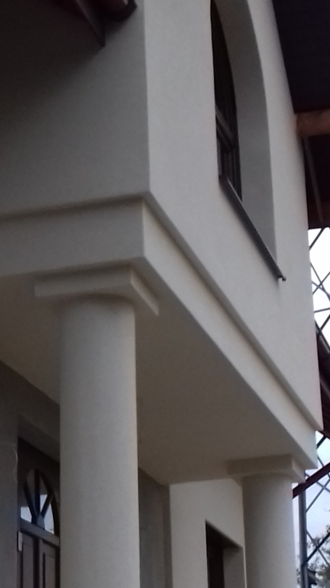 Wykończona elewacja budynku z kolumnami w Bochni. Widoczne detale architektoniczne i okno łukowe. Jasna kolorystyka elewacji.