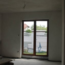 WITBUD - Wnętrze w stanie deweloperskim z oknem na ogród. Ściany przygotowane do malowania, widoczne kable i otwór wentylacyjny. Na podłodze wylewka.