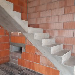 WITBUD - Betonowe schody w surowym stanie, w trakcie budowy, widoczne ceglane ściany i izolacja podłogi. Detal budowlany, etap prac wykończeniowych.