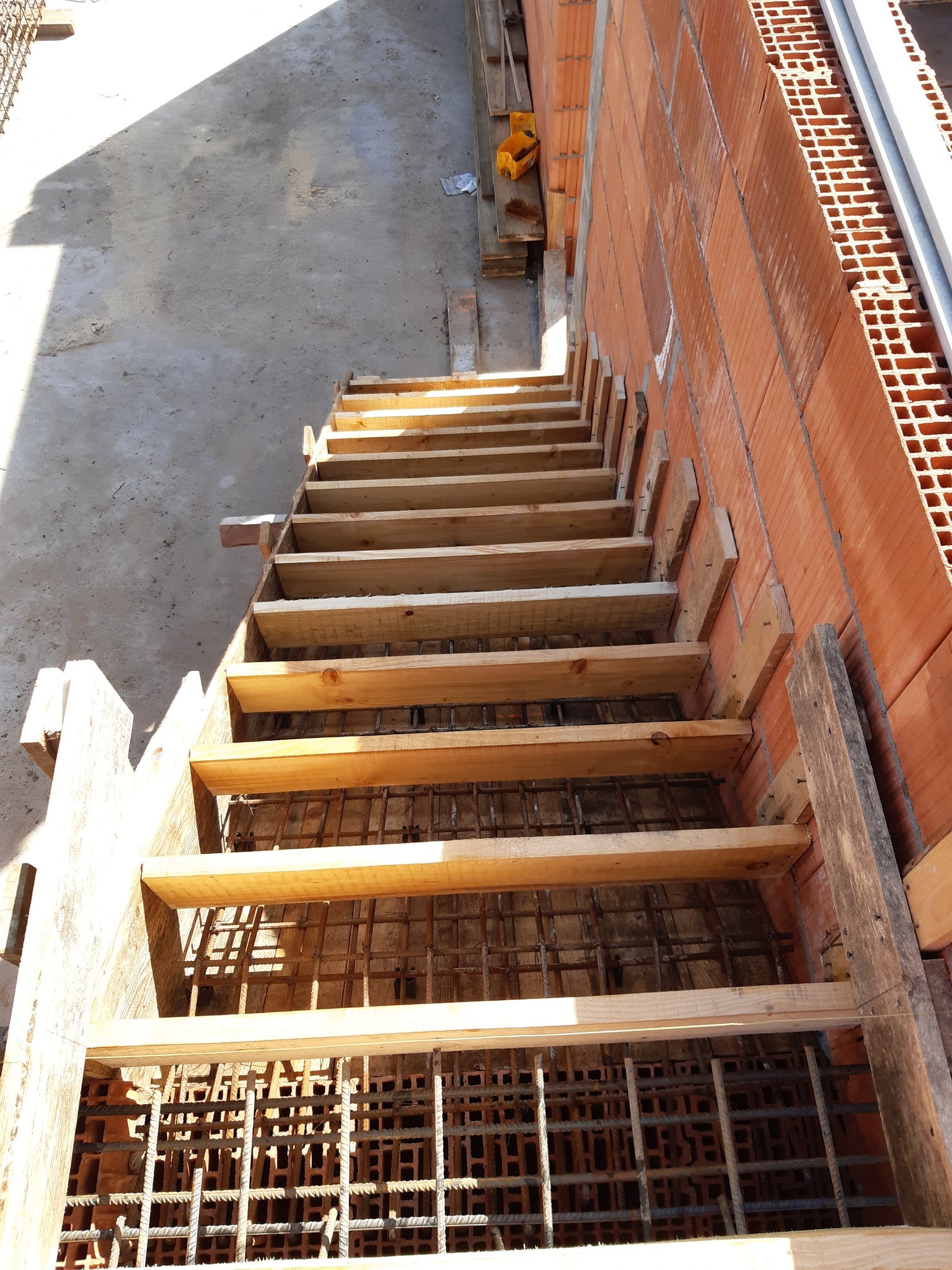 Szczegółowe ujęcie z góry na drewniane szalunki schodów zbrojonych, przylegających do ściany z czerwonej cegły dziurawki w surowym stanie.