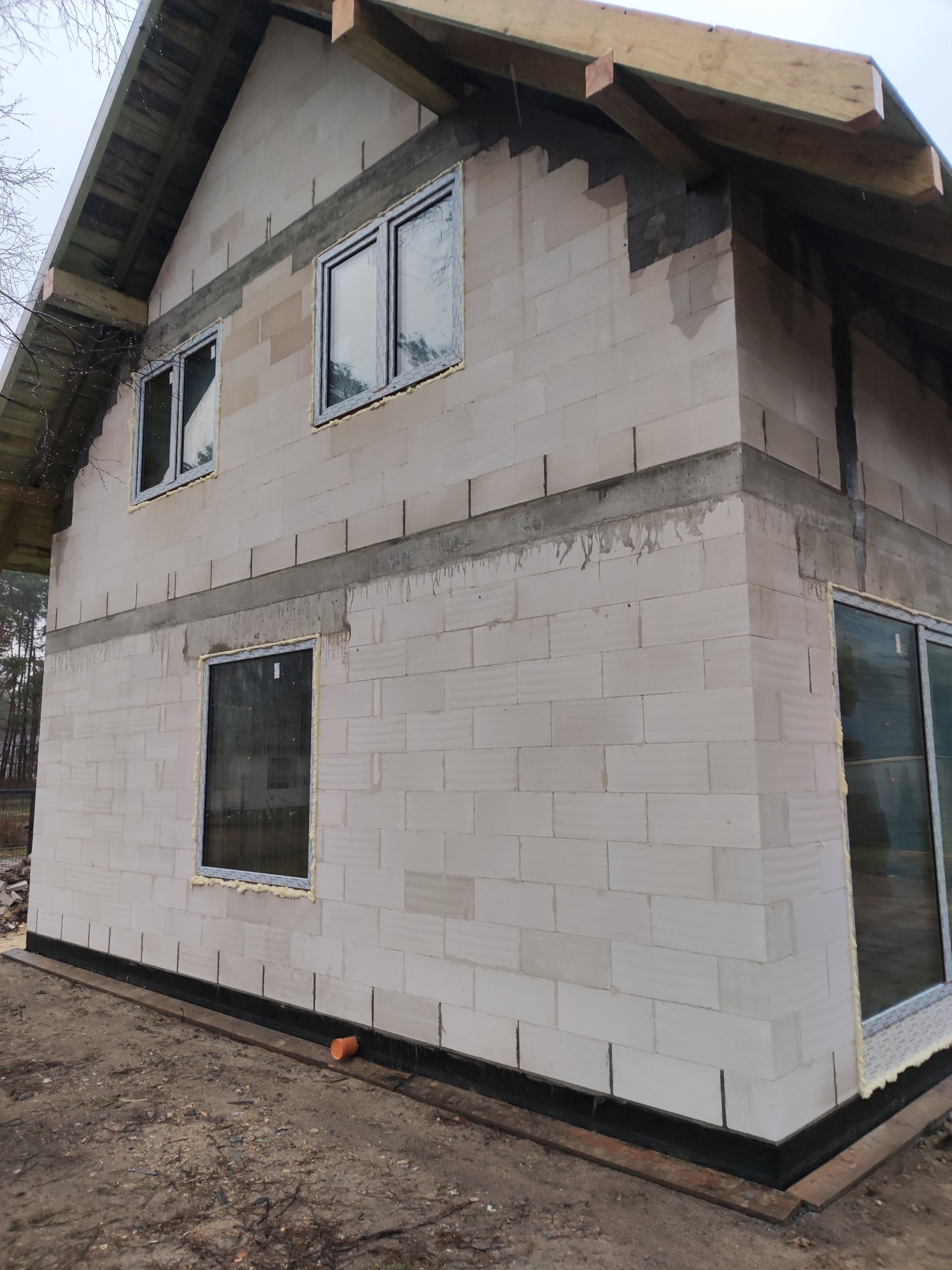 Budowa domu z betonu komórkowego w Piastowie, widoczne wstawione okna i elementy konstrukcji dachu. Stan surowy otwarty, ściany z betonu komórkowego.