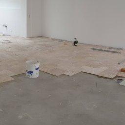 Dream Works Renovations - Układanie jasnych, kwadratowych płytek podłogowych w trakcie realizacji w Opolu. Widoczne narzędzia glazurnicze i częściowo ułożona podłoga w surowym wnętrzu.