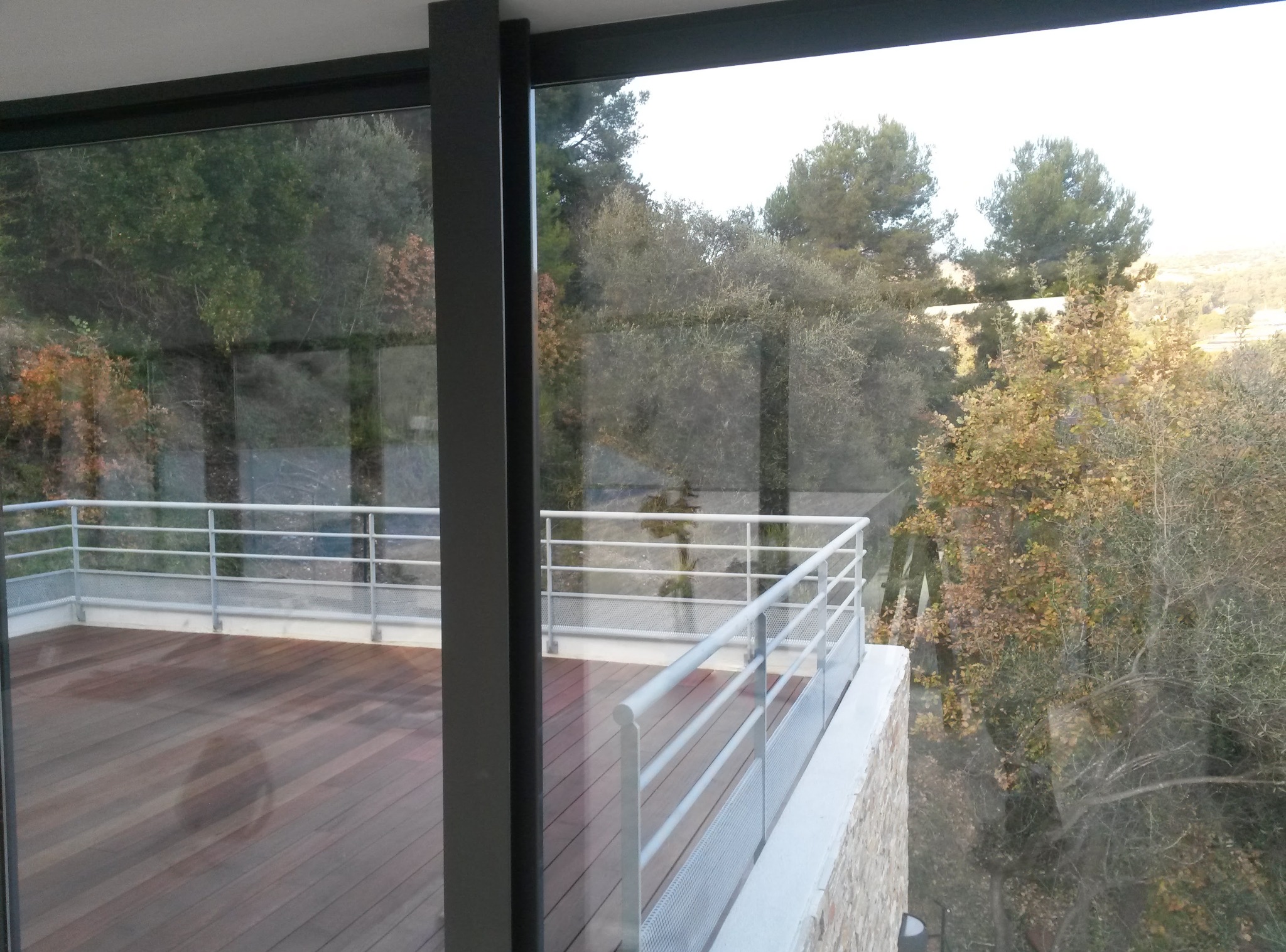 Nowoczesny balkon z drewnianą podłogą i metalową balustradą, widok przez okno na zieleń. Minimalistyczny design, jasne kolory, naturalne światło.