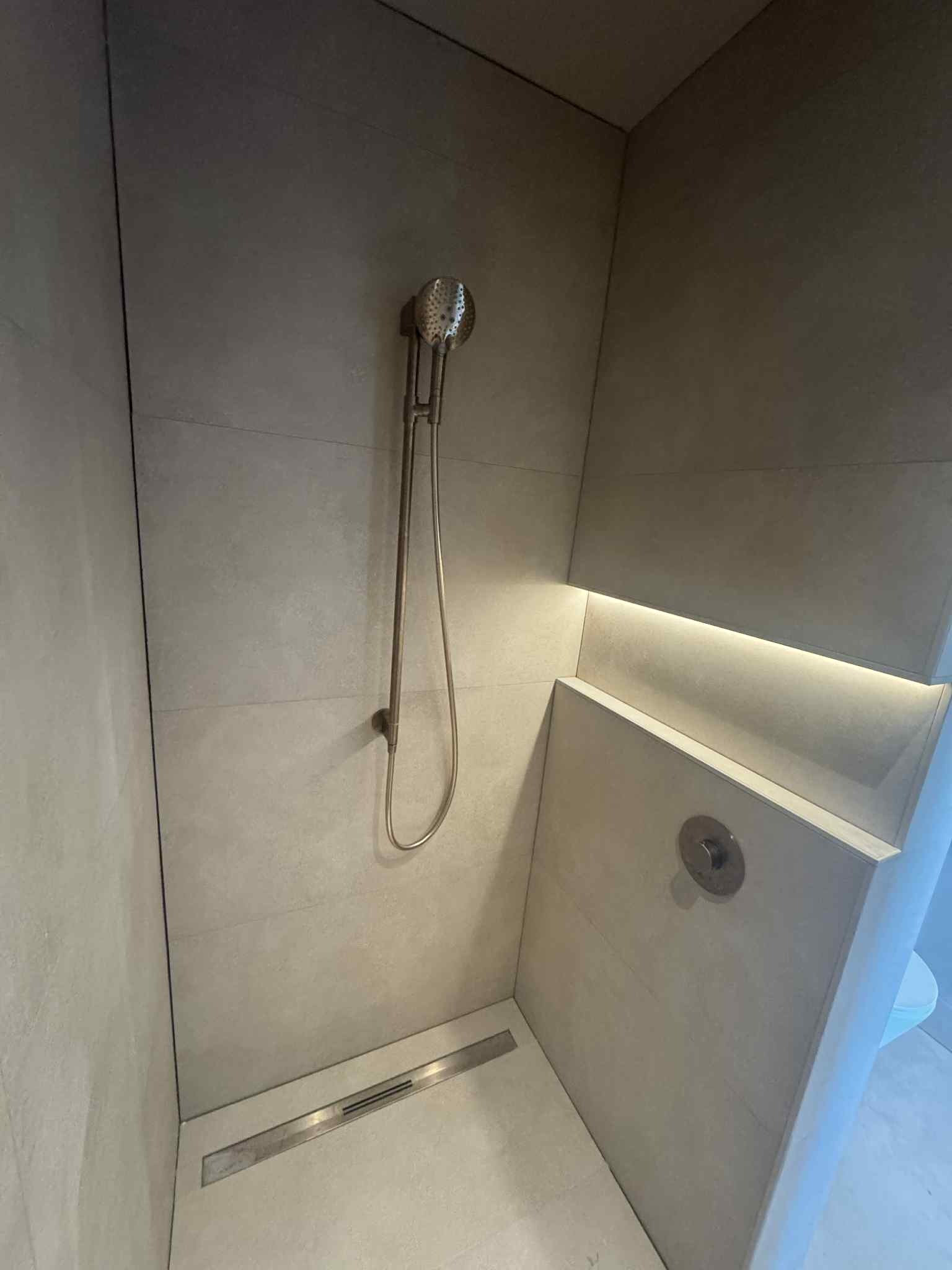 Nowoczesna kabina prysznicowa z odpływem liniowym, wykończona płytkami w odcieniach szarości i subtelnym oświetleniem LED. Minimalistyczny design.