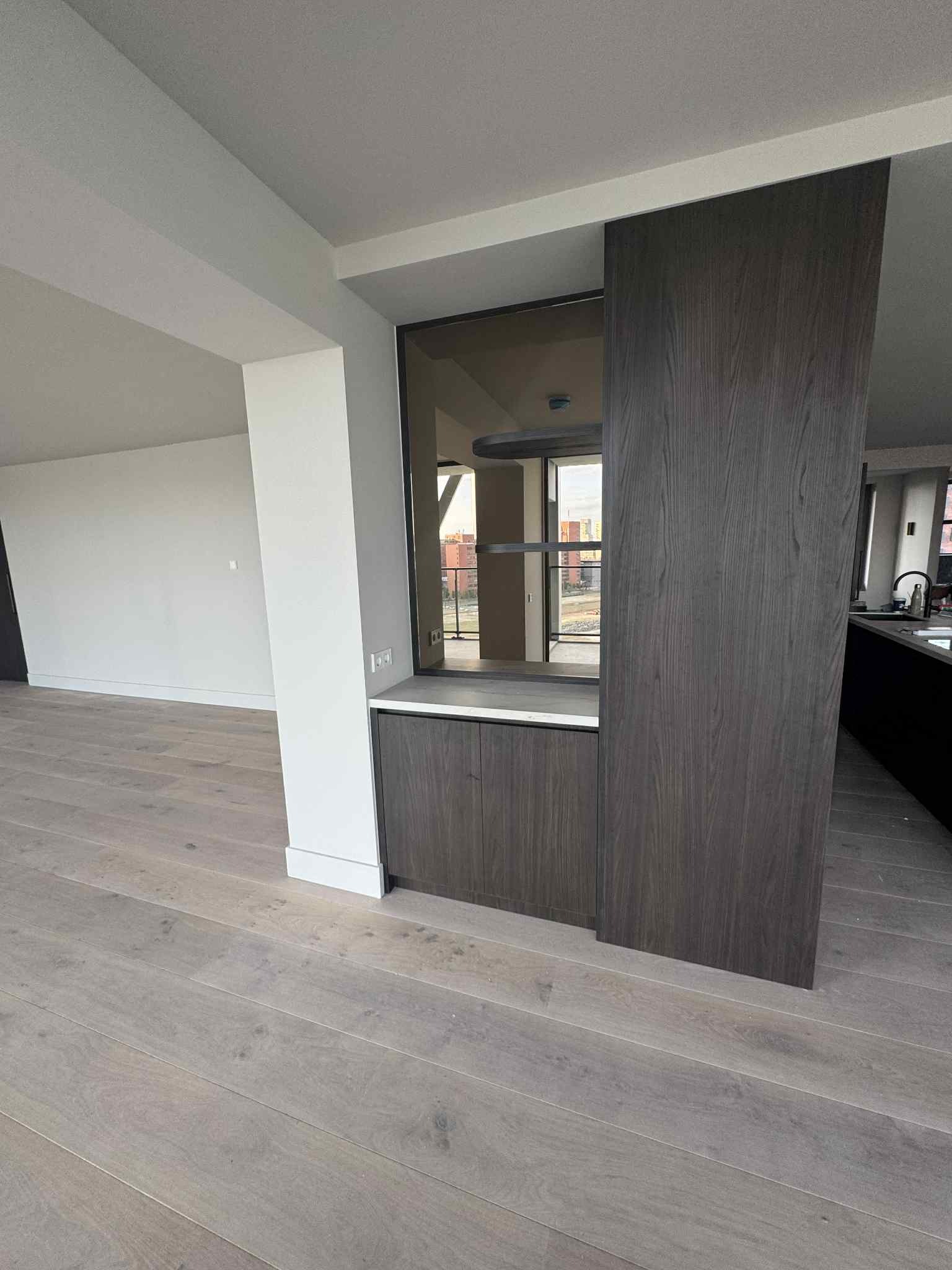 Nowoczesne wykończenie wnętrza: drewniana zabudowa z przeszkleniem, jasna podłoga i ściany. Minimalistyczny design z widokiem na zewnątrz.