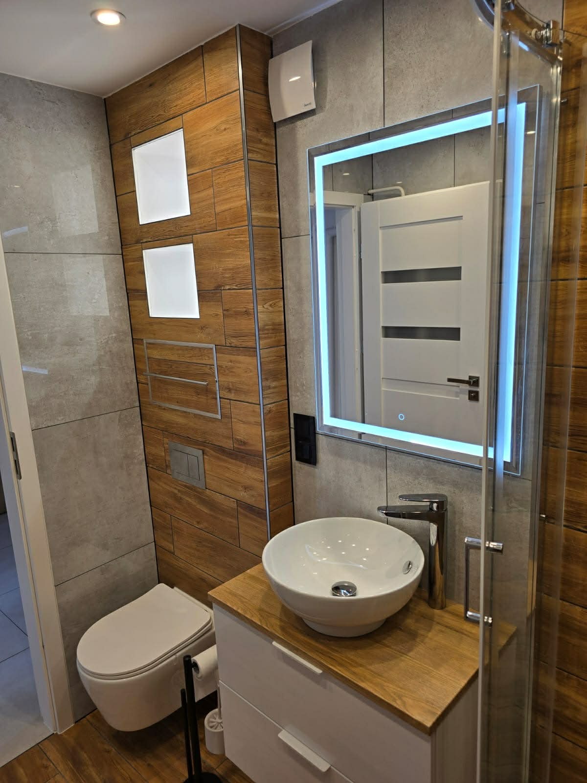Nowoczesna łazienka po remoncie: umywalka nablatowa, podświetlane lustro, drewnopodobne płytki, wisząca toaleta. Wykończenie wnętrz z dbałością o detale.