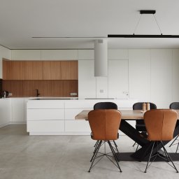 NOWATOM Tomasz Międła - Nowoczesna kuchnia z drewnianymi akcentami i stołem jadalnym. Minimalistyczny design, jasne kolory, geometryczne lampy. Widok na okno z zasłonami.