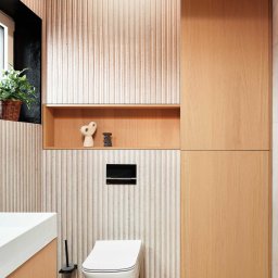 NOWATOM Tomasz Międła - Nowoczesna łazienka z toaletą podwieszaną, umywalką z szafką i ścianą z dekoracyjnymi panelami. Drewniane akcenty i minimalistyczne dodatki.