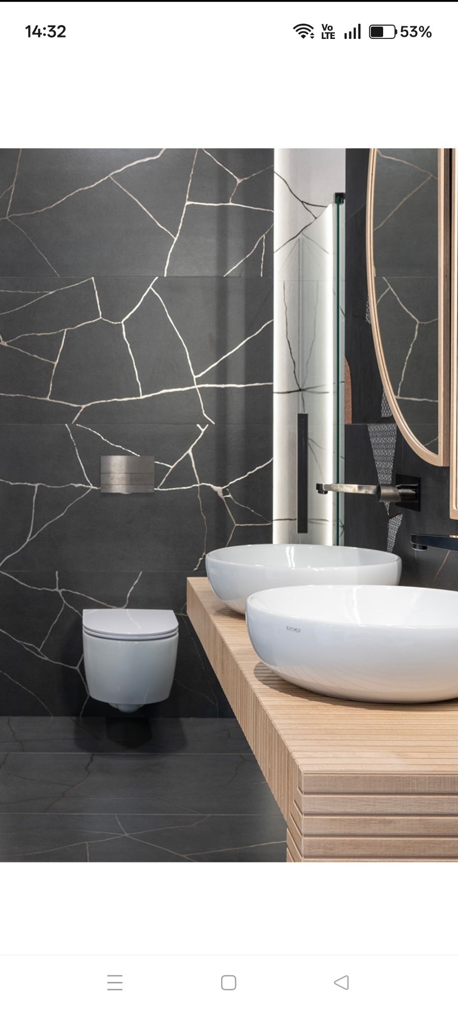 Nowoczesna łazienka z czarnymi płytkami imitującymi marmur ze złotymi żyłami, dwie białe umywalki na drewnianym blacie i podwieszana toaleta.