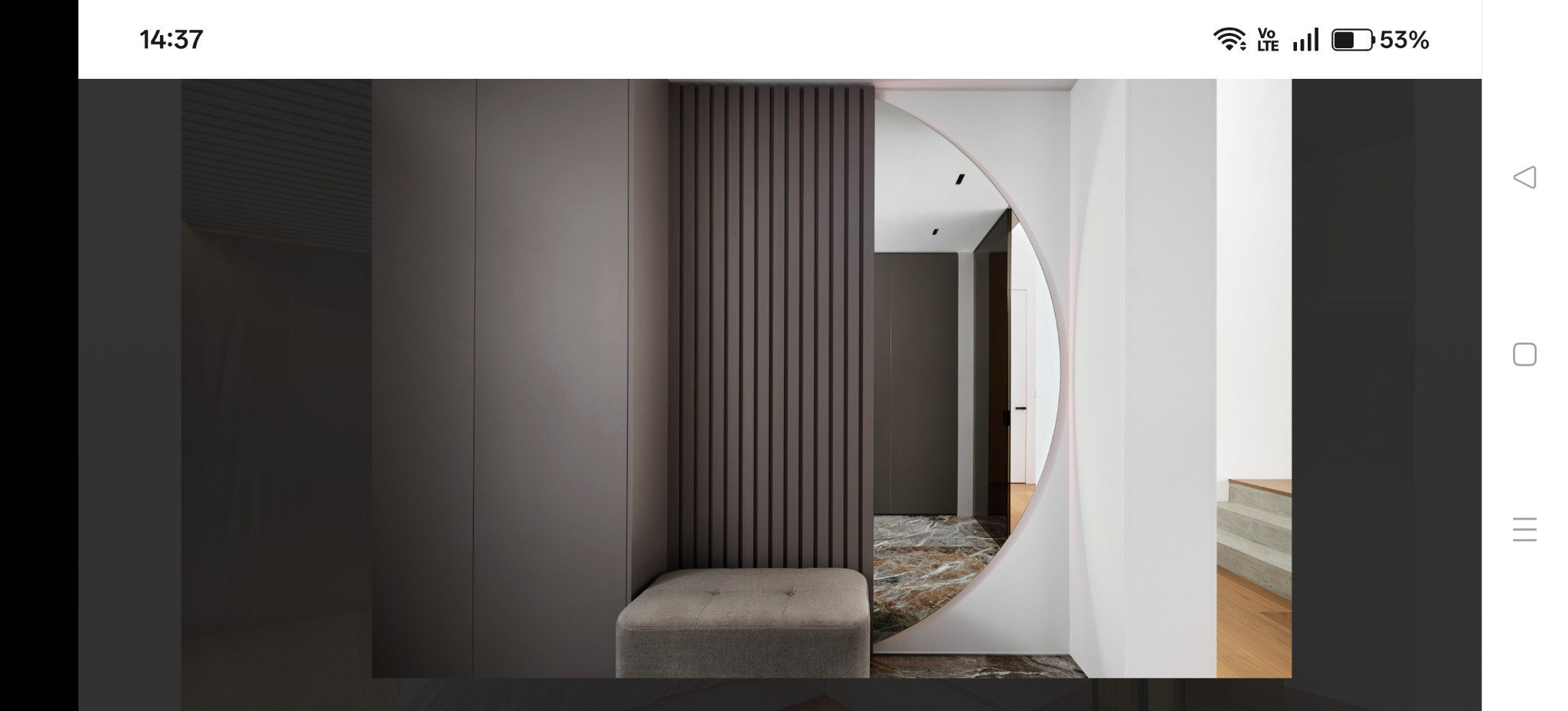 Nowoczesny przedpokój z szarą zabudową, panelem ściennym i okrągłym przejściem. Marmurowa podłoga i pufa dodają elegancji. Minimalistyczny design.