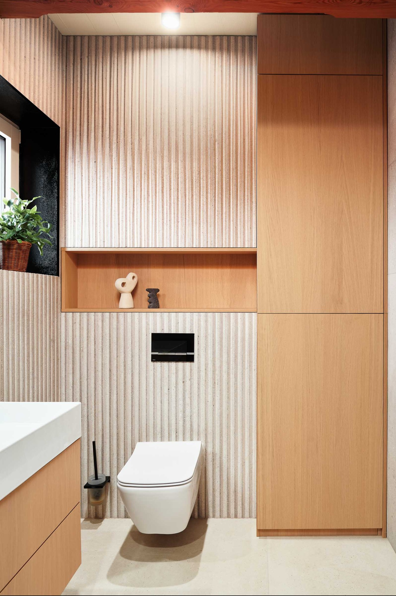 Nowoczesna łazienka z toaletą podwieszaną, umywalką z szafką i ścianą z dekoracyjnymi panelami. Drewniane akcenty i minimalistyczne dodatki.