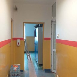 STRATUM GROUP - Korytarz po malowaniu ścian na żółto i biało z czerwonym paskiem. Na podłodze wzór w kwadraty. Widoczny dozownik i butelki z wodą.