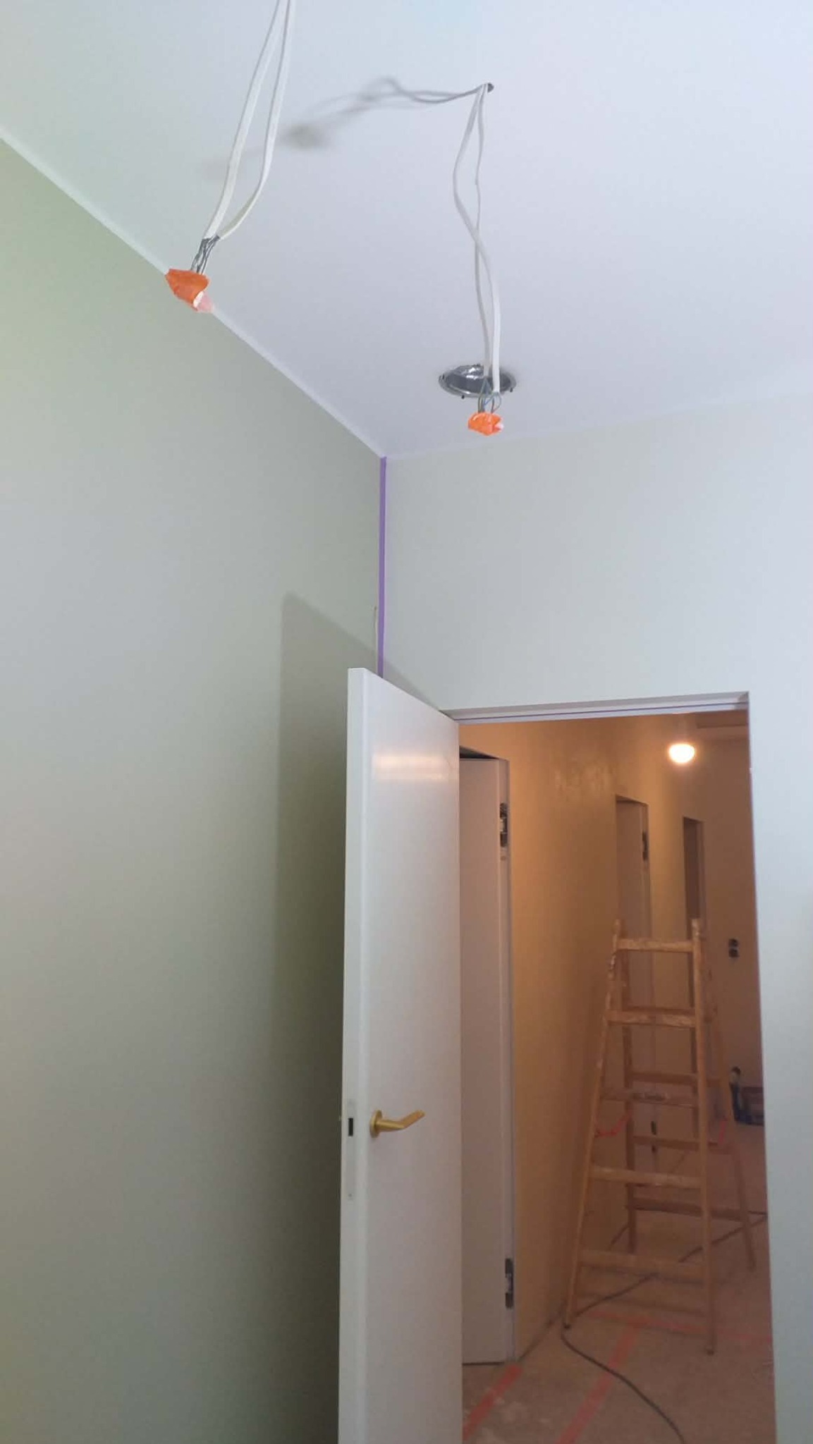 Wnętrze w trakcie prac wykończeniowych: świeżo pomalowane ściany w odcieniach szarości, widoczne przewody elektryczne wystające z sufitu, otwarta biała stolarka drzwiowa.