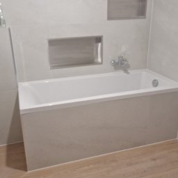 Remonty wykonczenia Krzysztof Barciszewski - Wykończona łazienka z wanną w zabudowie, jasnymi płytkami i drewnopodobną podłogą. W ścianie wnęki wykończone płytkami. Minimalistyczny design.