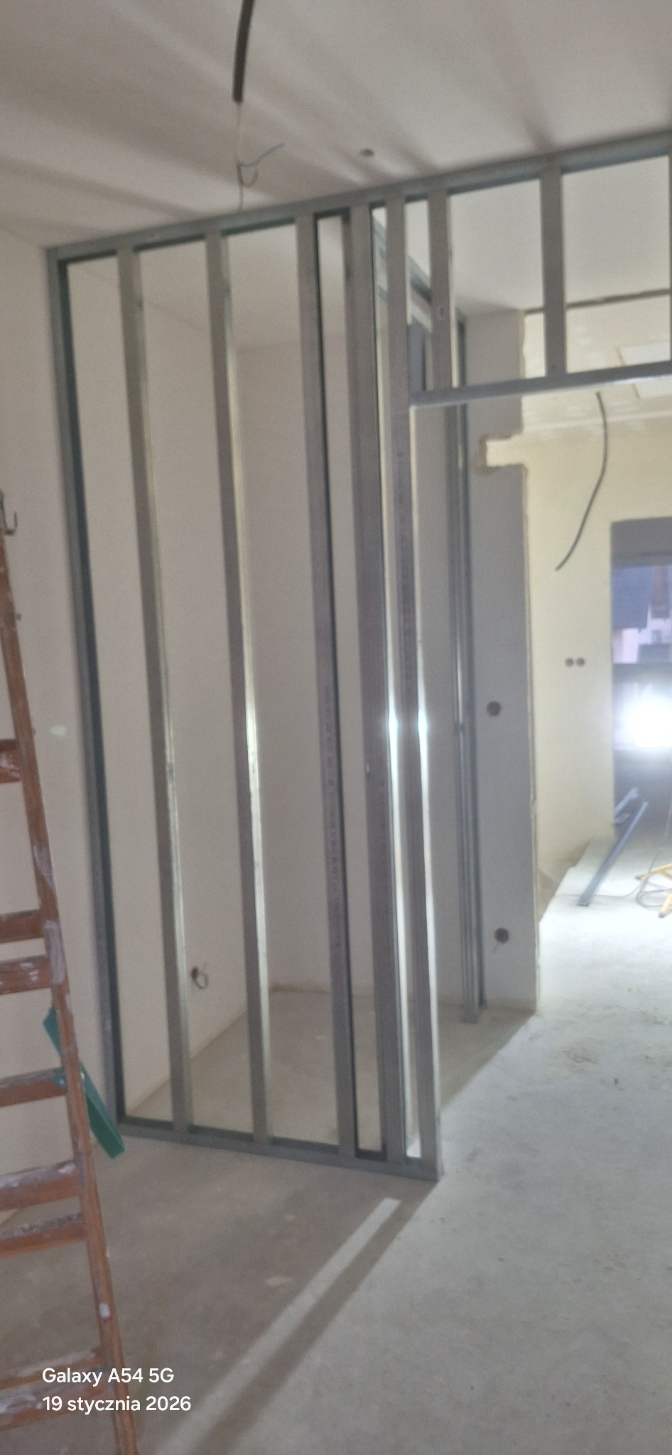 Konstrukcja ścianki działowej z profili metalowych w trakcie montażu. Widoczna drabina i surowy stan wnętrza. Prace przygotowawcze do zabudowy.