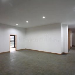 Konrad Walczy - Puste, jasne wnętrze po remoncie: gładkie, białe ściany, szara podłoga z płytek, widoczne drzwi i okna. Minimalistyczny styl, równomierne oświetlenie punktowe.