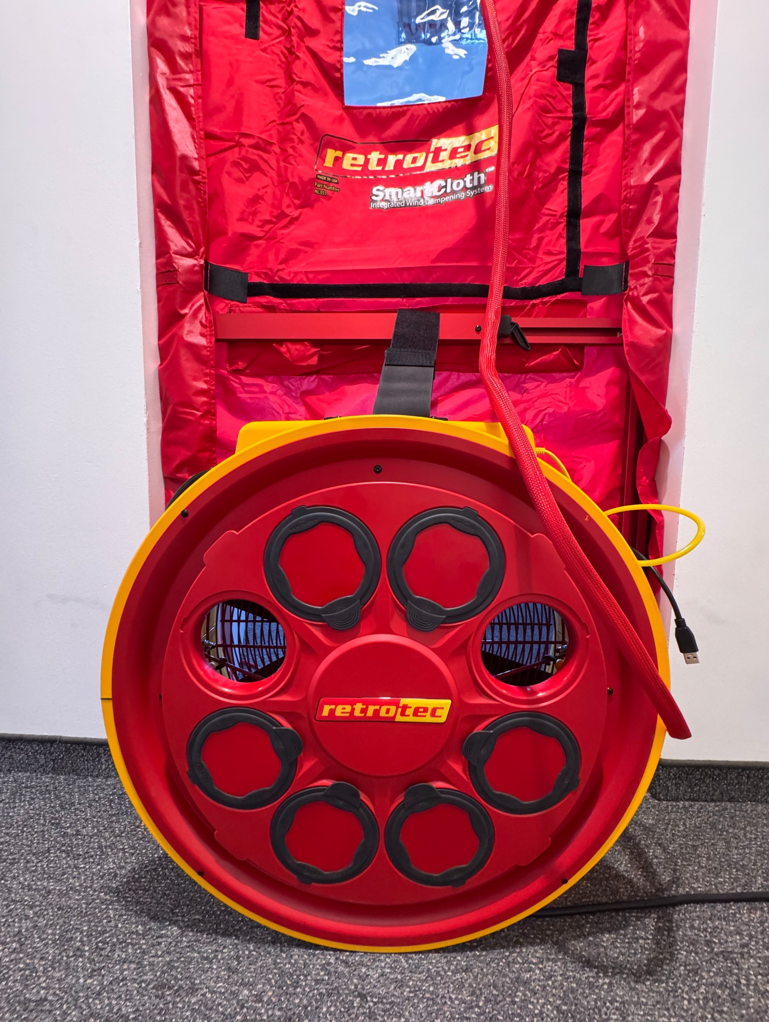 Sprzęt Retrotec do testu szczelności budynku (Blower Door Test): czerwono-żółty wentylator z osłoną na tle białej ściany i czerwonej płachty uszczelniającej.