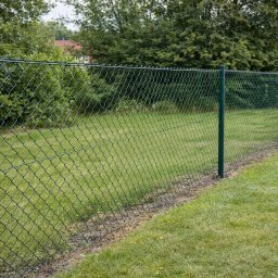 Polstal - Zielona siatka ogrodzeniowa z metalowymi słupkami na trawniku, widok z boku. W tle drzewa i fragment dachu budynku.