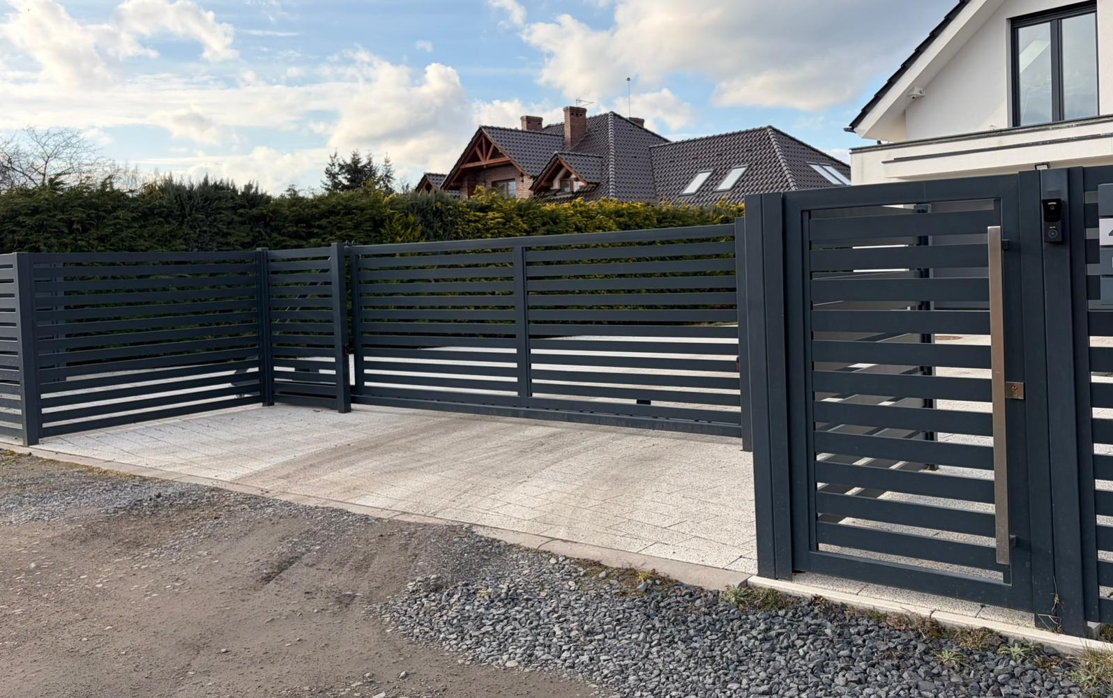 Nowoczesna, pozioma brama przesuwna z metalu w kolorze antracytu, z widocznym panelem sterowania i uchwytem, na tle domu z ogrodem.