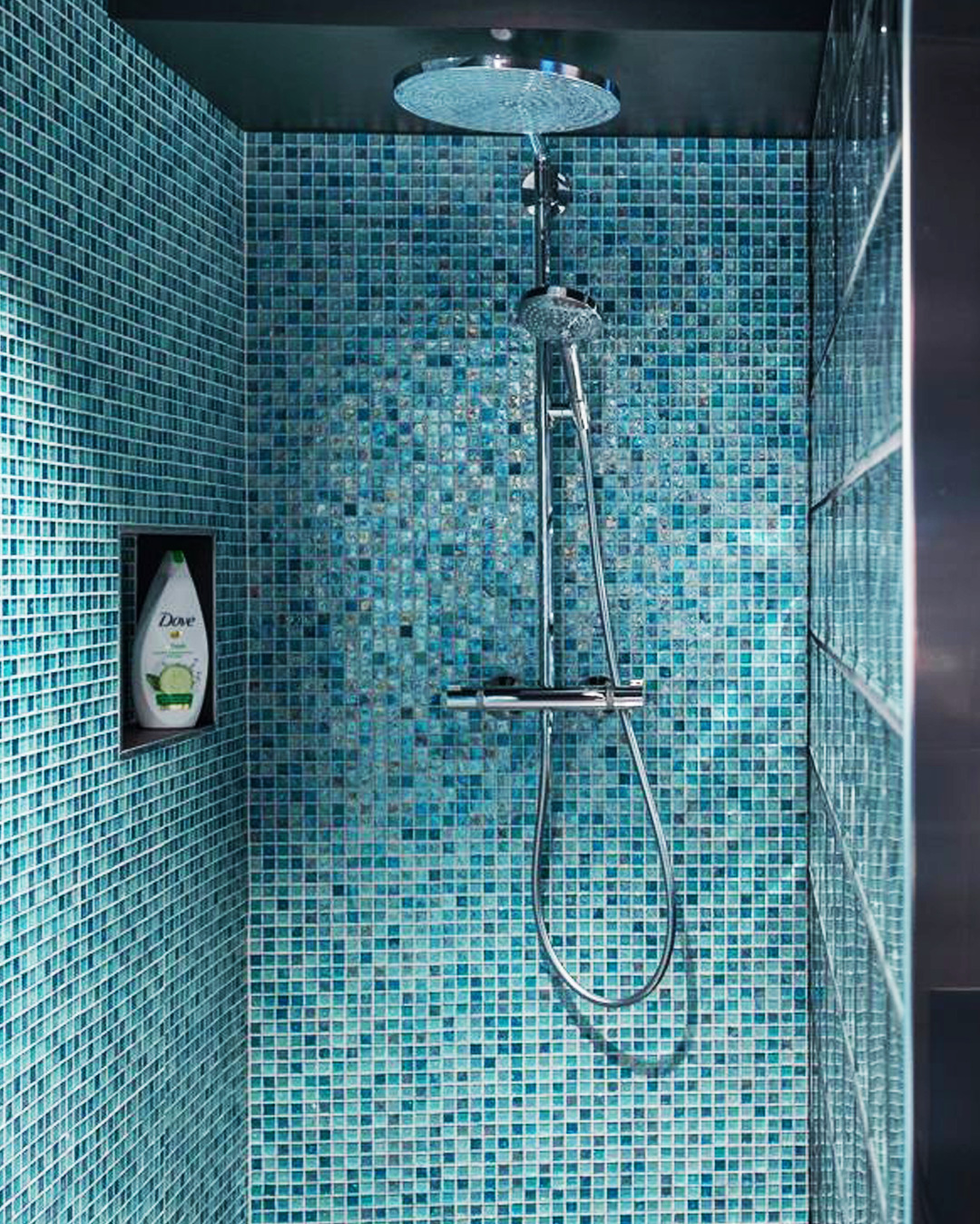 Kabina prysznicowa wyłożona mozaiką w odcieniach błękitu i turkusu. Widoczna bateria, deszczownica i wnęka z kosmetykiem. Nowoczesny design, precyzyjne ułożenie płytek.