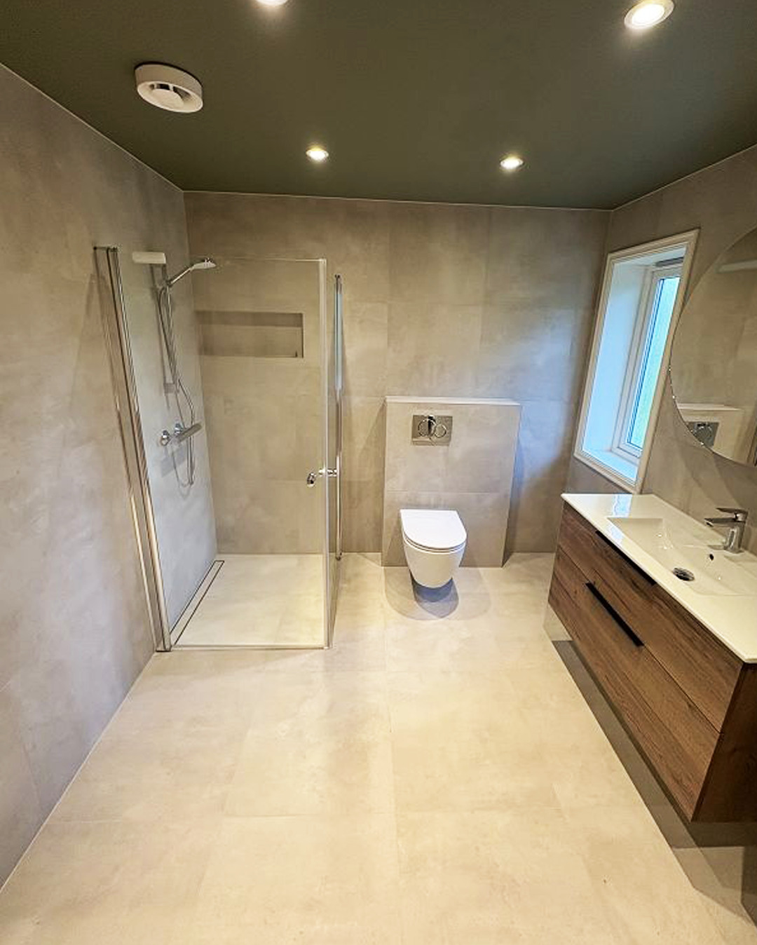 Jasna łazienka z kabiną prysznicową, toaletą i umywalką z drewnianą szafką. Sufit w kolorze oliwkowym. Minimalistyczny design, neutralna kolorystyka.