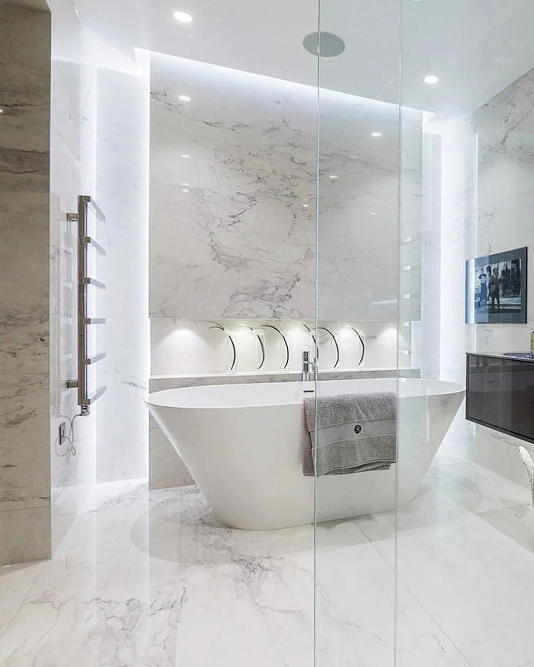 Elegancka, marmurowa łazienka z wolnostojącą wanną, szklaną kabiną prysznicową i podświetleniem LED. Minimalistyczny design z akcentami chromu i szarości.