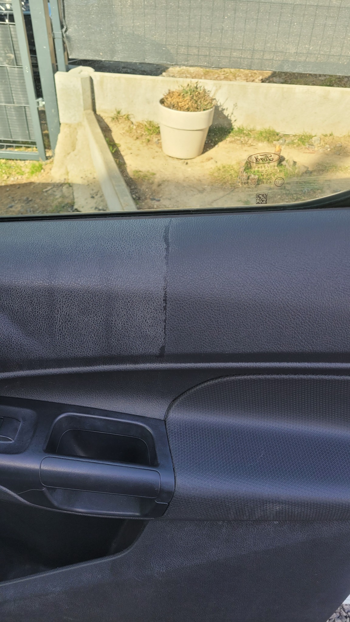 Wnętrze samochodu: czyszczone drzwi od wewnątrz, widoczna różnica przed i po czyszczeniu. Na zewnątrz przez szybę widać roślinę w doniczce.