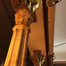 Wentica Tomasz Manowski - Antyczna kolumna z dekoracyjną głowicą sąsiaduje z nowoczesną rurą wentylacyjną pod sufitem, oświetloną punktowym światłem. Kontrast stylów i epok.