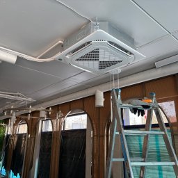 Wentica Tomasz Manowski - Sufitowa klimatyzacja kasetonowa w jasnym wnętrzu, widoczna drabina i instalacje. Ujęcie z dołu, podkreślające nowoczesny design urządzenia.