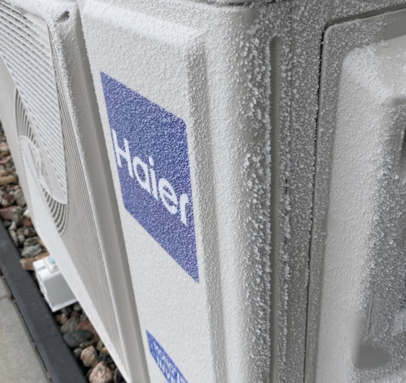 Zaszroniony agregat klimatyzacji Haier w Pruszczu Gdańskim. Widoczne kryształki lodu na obudowie i logo. Niska temperatura otoczenia.