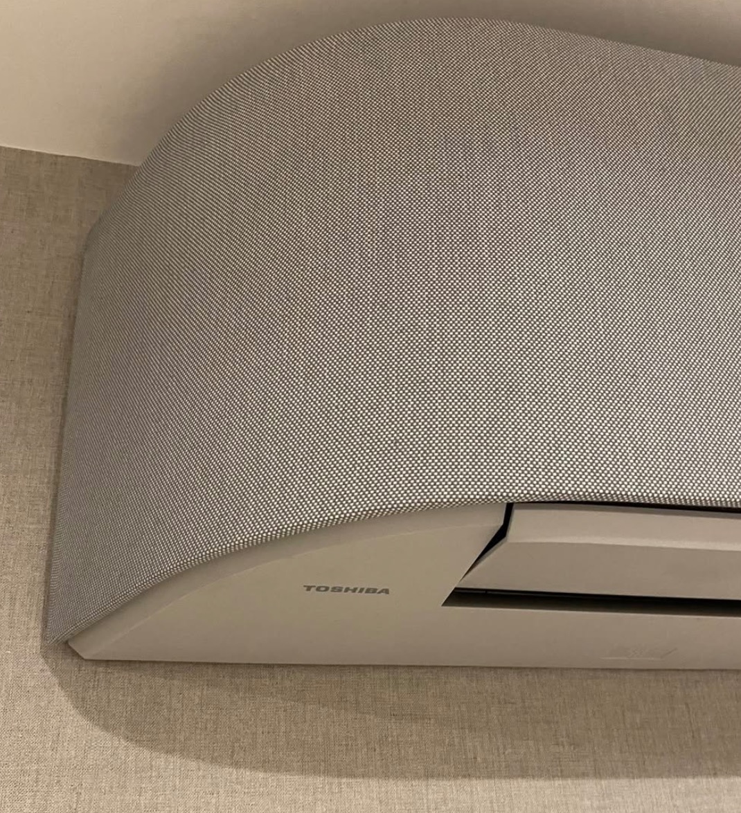 Szary klimatyzator Toshiba z unikalną, teksturowaną obudową, zamontowany na ścianie o delikatnej fakturze. Widoczny fragment sufitu.