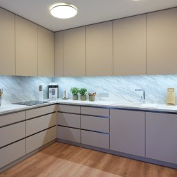 Karol Dyduch - Nowoczesna kuchnia z beżowymi szafkami, marmurowym blatem i podświetleniem LED. Minimalistyczny design z drewnianą podłogą i wbudowanym sprzętem AGD.