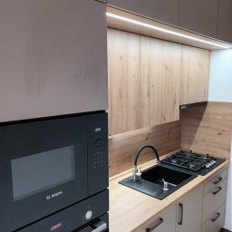 Karol Dyduch - Nowoczesna kuchnia z beżowymi szafkami, drewnianym blatem i czarnym zlewem. W zabudowie piekarnik i mikrofalówka marki Bosch. Oświetlenie LED podszafkowe.