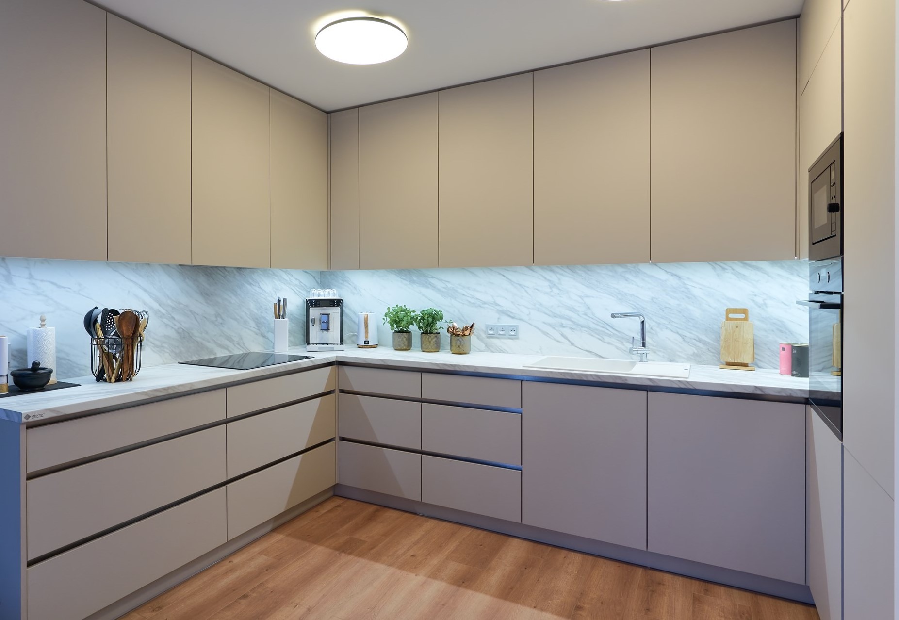 Nowoczesna kuchnia z beżowymi szafkami, marmurowym blatem i podświetleniem LED. Minimalistyczny design z drewnianą podłogą i wbudowanym sprzętem AGD.