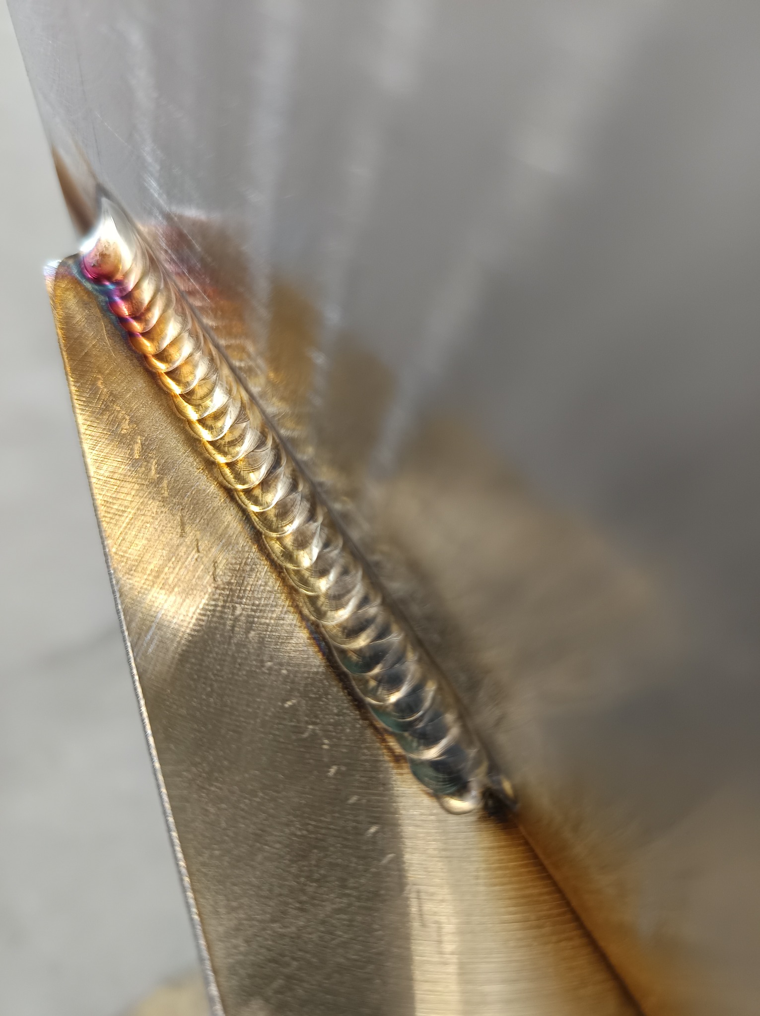 Precyzyjne spawy na metalowej powierzchni, widoczne detale łączenia z charakterystycznymi kolorami termicznymi. Ukazane z bliska, podkreślając jakość wykonania.