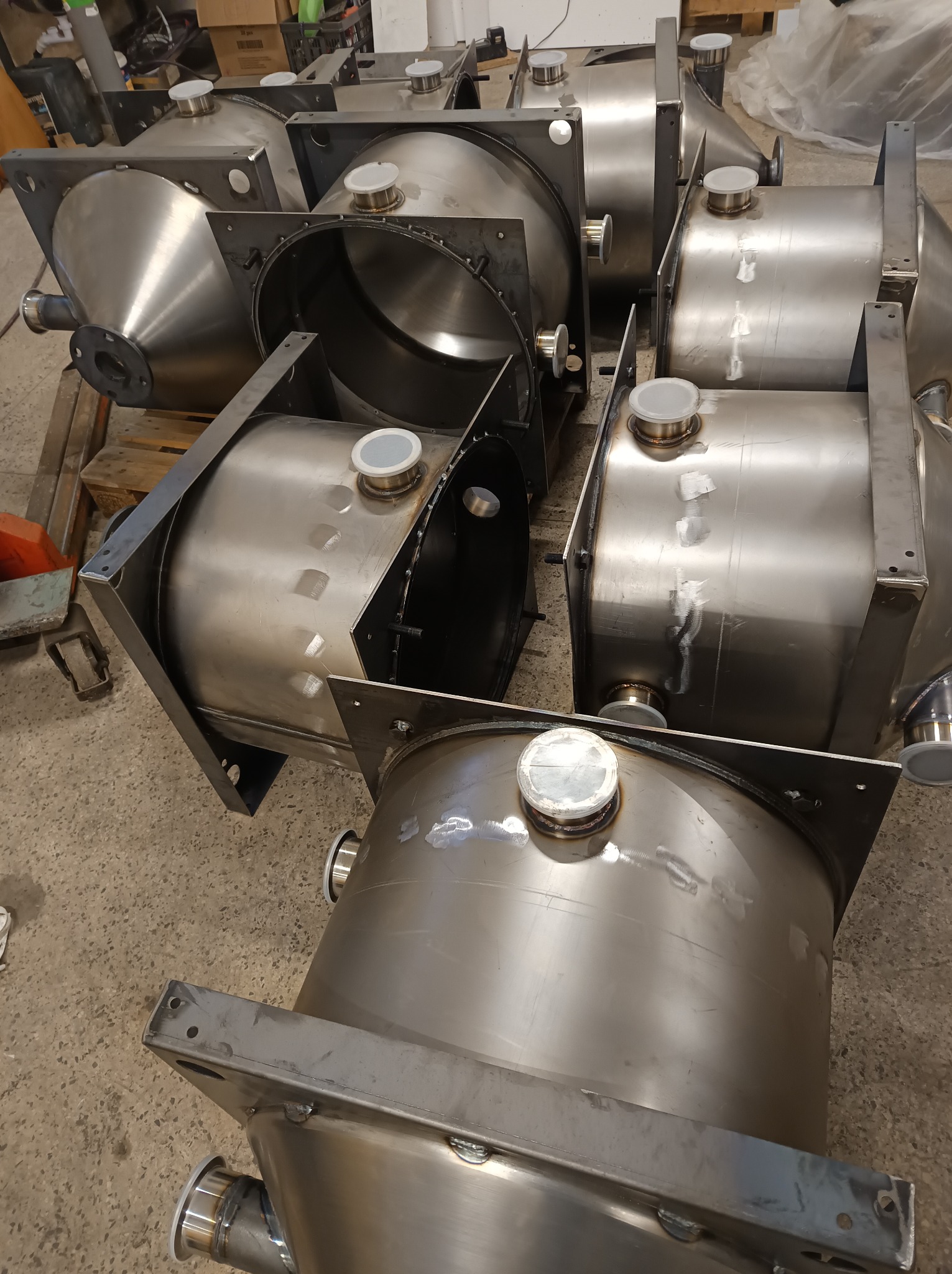 Metalowe zbiorniki ze stali nierdzewnej, ustawione na podłodze warsztatu, gotowe do dalszej obróbki lub montażu. Widoczne spawy i elementy konstrukcyjne.