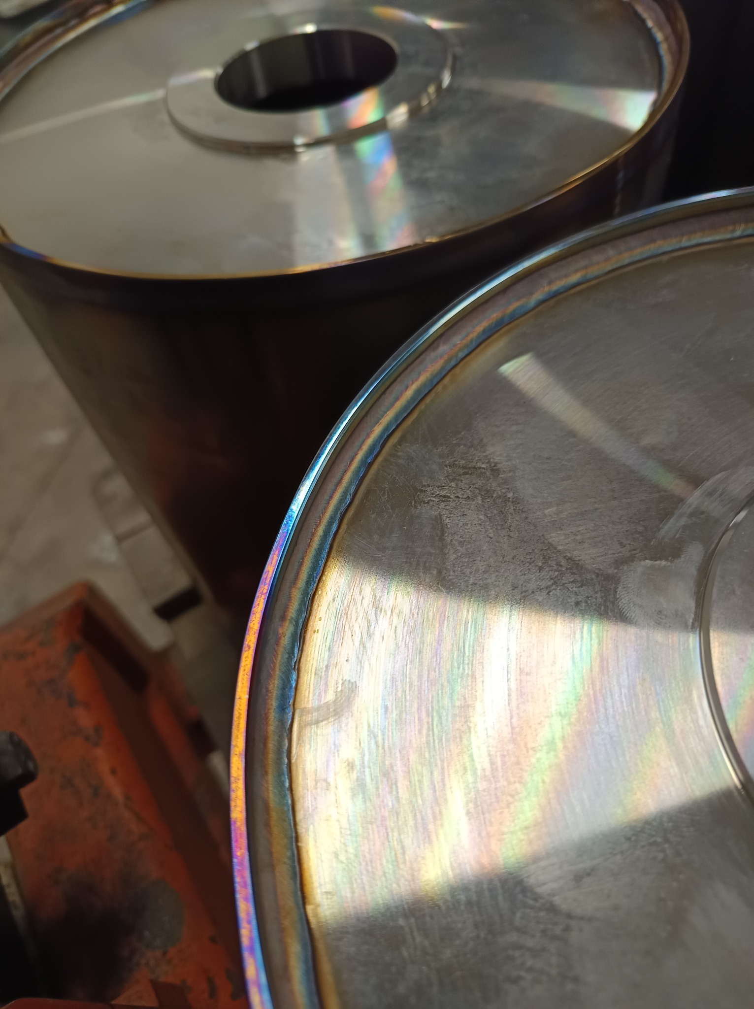 Dwa metalowe cylindryczne elementy po obróbce w Lubaniu, widoczne ślady spawania i opalizujące kolory na krawędziach. Detal obróbki metalu.