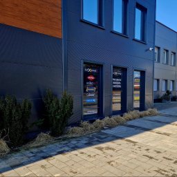 LUXNAR SPÓŁKA Z OGRANICZONĄ ODPOWIEDZIALNOŚCIĄ - Nowoczesny budynek firmy Luxnar z logo marek narzędzi (Knipex, Wiha, Hazet, Vigor, Hogert) na witrynach. Widok z zewnątrz, kostka brukowa, krzewy.